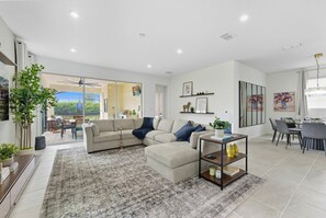 A modern living room with a sectional sofa, a coffee table, and a dining area with a table and chairs. - 7BR Solara Themed Rooms, Cinema, Pool & spa (Kissimmee)