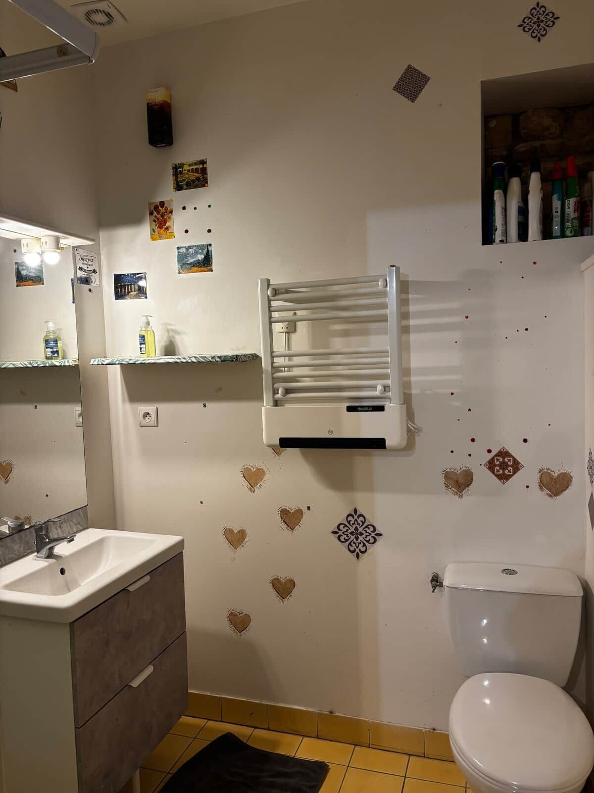 A bathroom with a white sink, mirror, and toilet. There are heart-shaped decorations on the wall and a towel rack above the sink.
