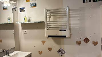 A bathroom with a white sink, mirror, and toilet. There are heart-shaped decorations on the wall and a towel rack above the sink.