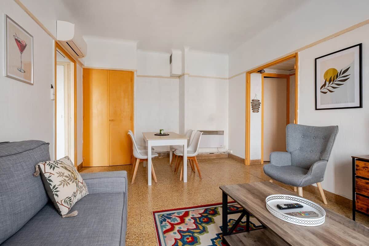 Una sala de estar moderna con un sofá gris, una mesa de comedor con sillas, un sillón gris y una mesita de centro con una bandeja.