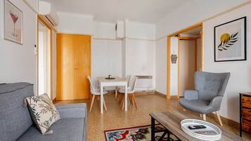 Una sala de estar moderna con un sofá gris, una mesa de comedor con sillas, un sillón gris y una mesita de centro con una bandeja.