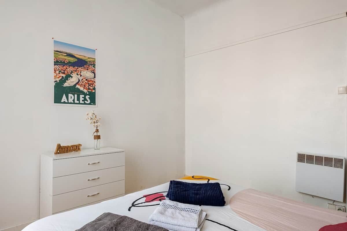 A bedroom with a bed, a dresser, a poster on the wall, and a radiator.