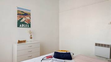 A bedroom with a bed, a dresser, a poster on the wall, and a radiator.