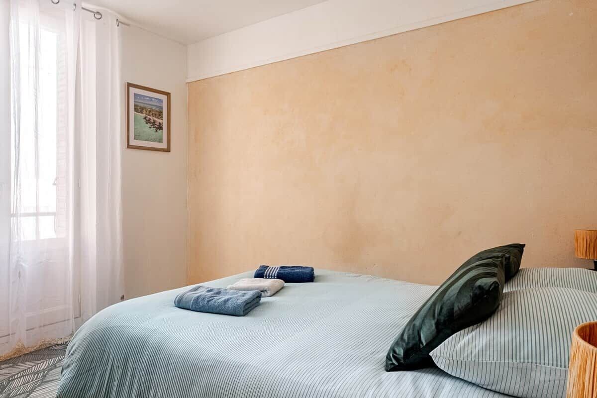 Un dormitori amb un llit, almoines, un quadre al mur i una finestra amb cortines.