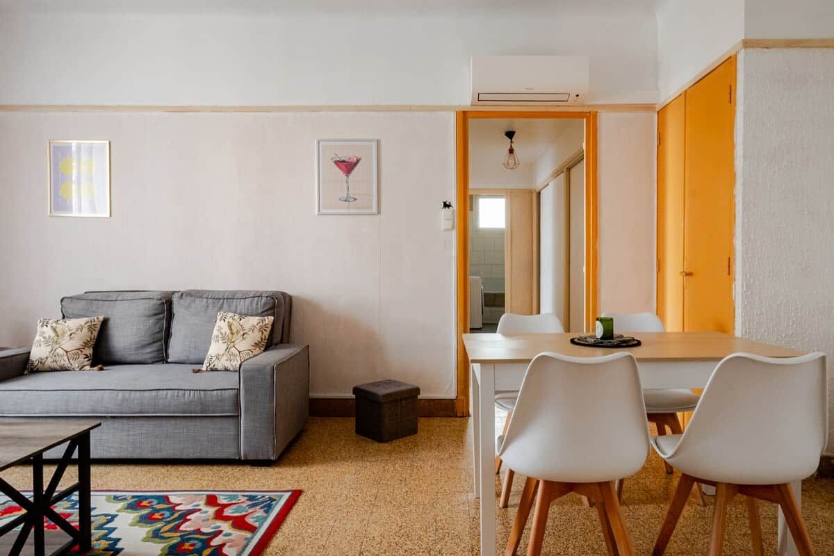 Una sala de estar moderna con un sofá gris, sillas blancas, una mesita y un tapete colorido.