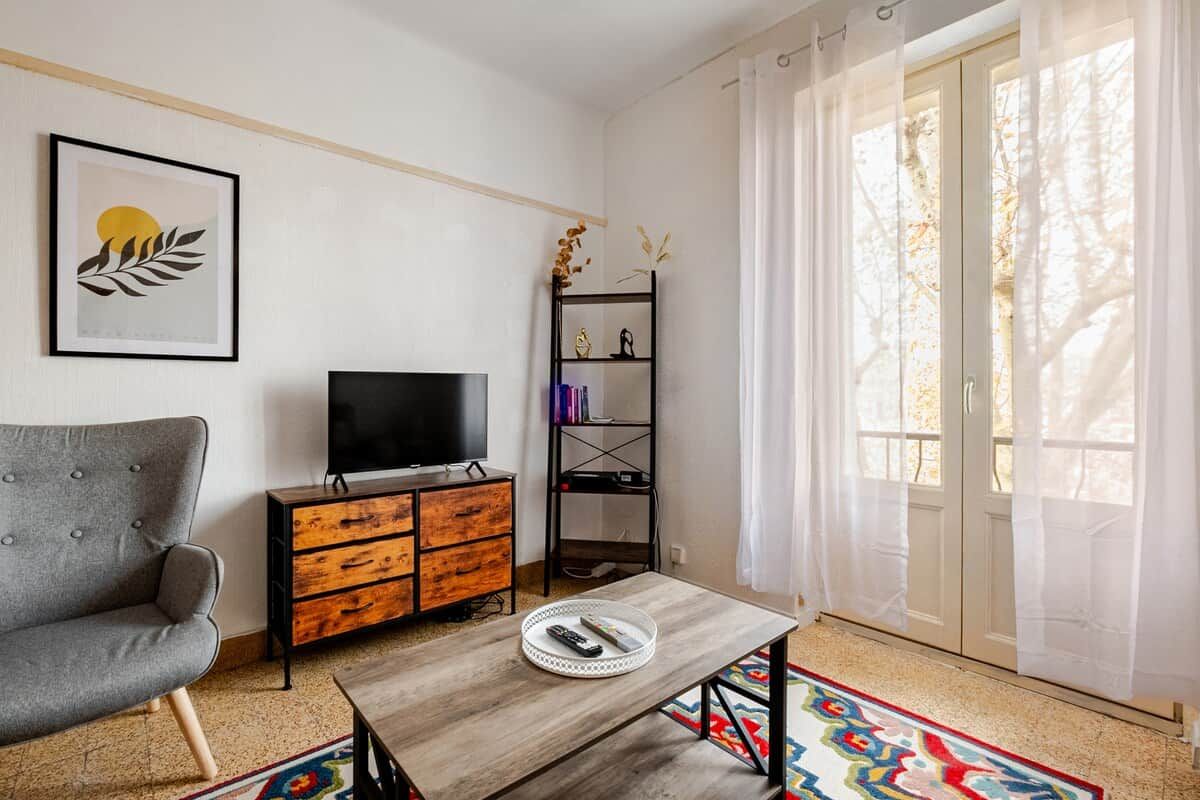 Una sala de estar con un sofá, un televisor sobre un mueble de madera, una mesa de centro y una estantería.