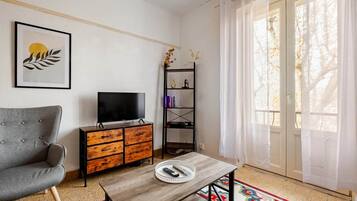 Una sala de estar con un sofá, un televisor sobre un mueble de madera, una mesa de centro y una estantería.