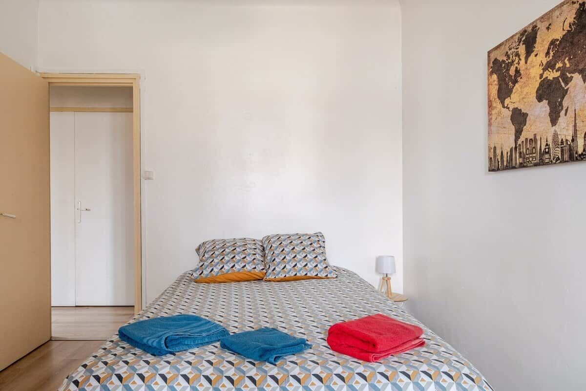 Un dormitorio con cama, almohadas y una manta. Hay una puerta y una pared con un cuadro.