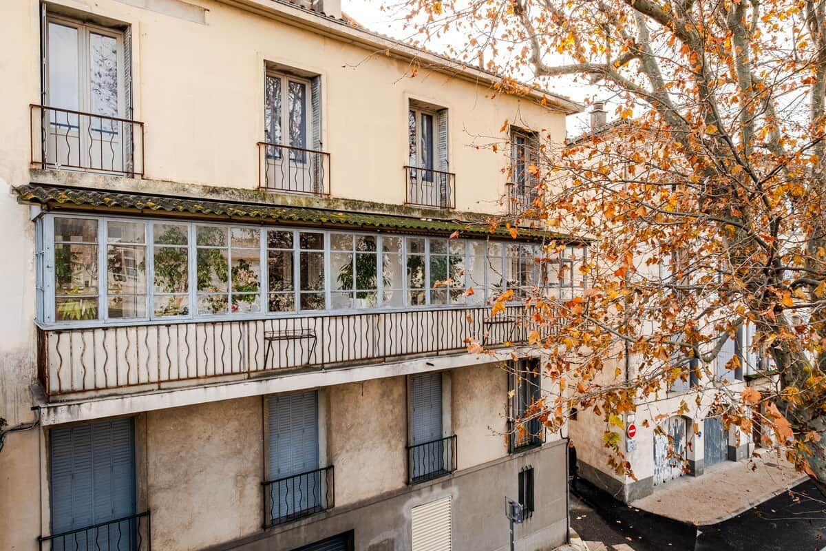 A multi-story building with balconies, windows, and a tree with autumn leaves.