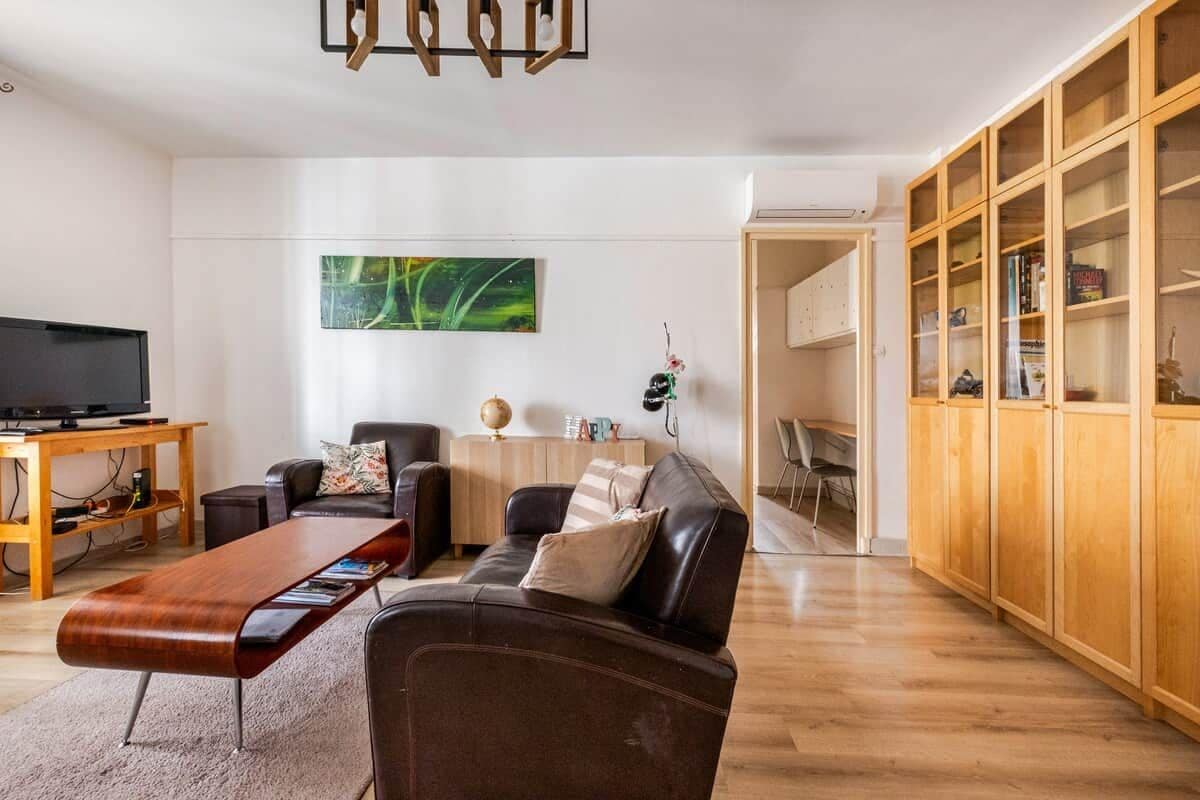 A modern living room with a leather sofa, a wooden coffee table, a flat-screen TV, and a bookshelf.