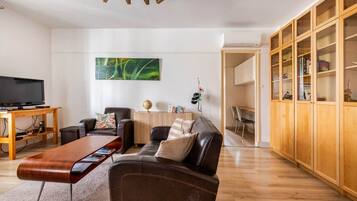 A modern living room with a leather sofa, a wooden coffee table, a flat-screen TV, and a bookshelf.