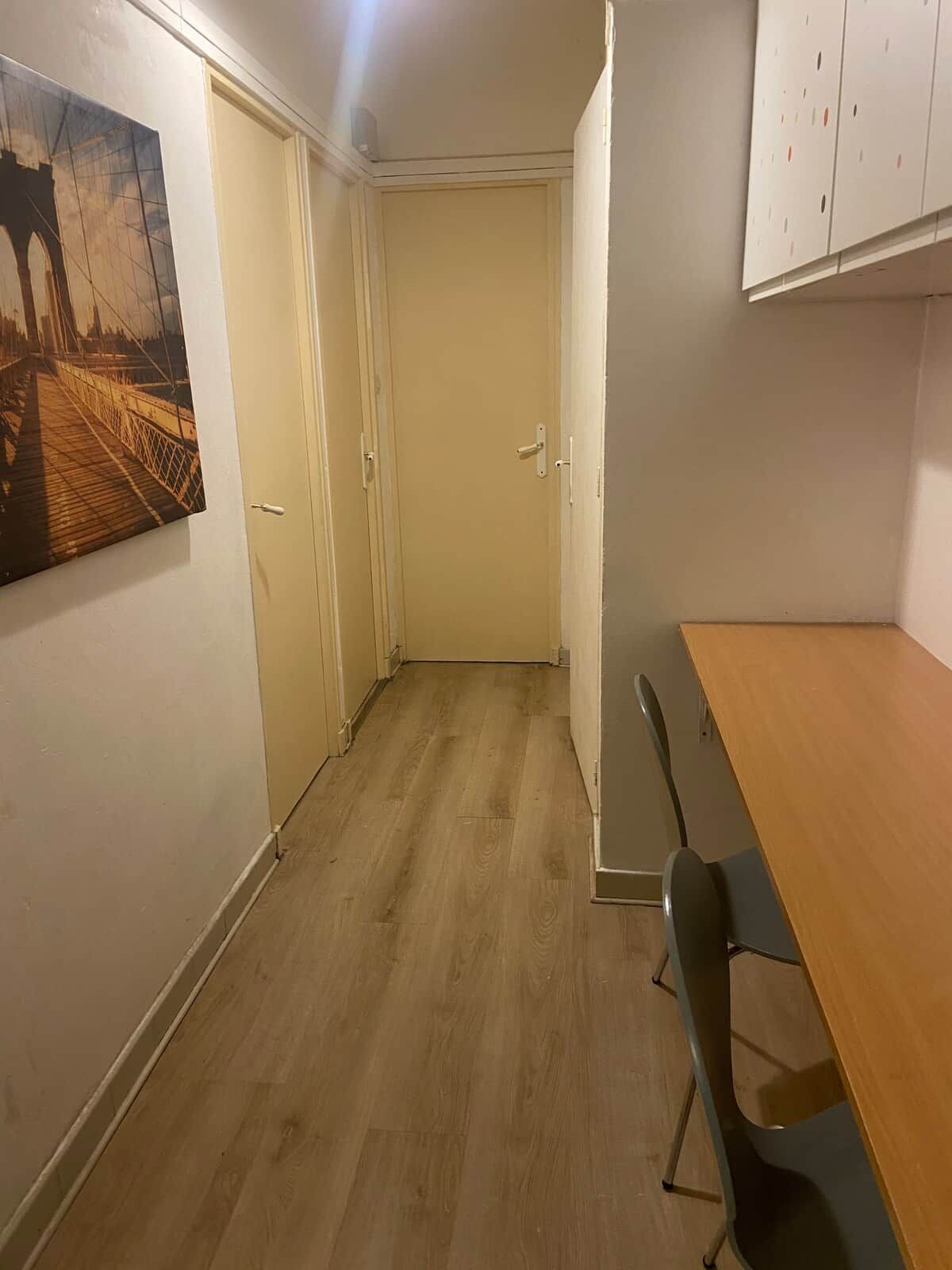 A hallway with a wooden floor, a painting on the wall, and a door at the end.