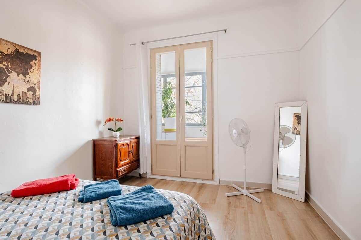 Un dormitorio con cama, cómoda, ventilador, espejo y puerta que da a un espacio exterior.
