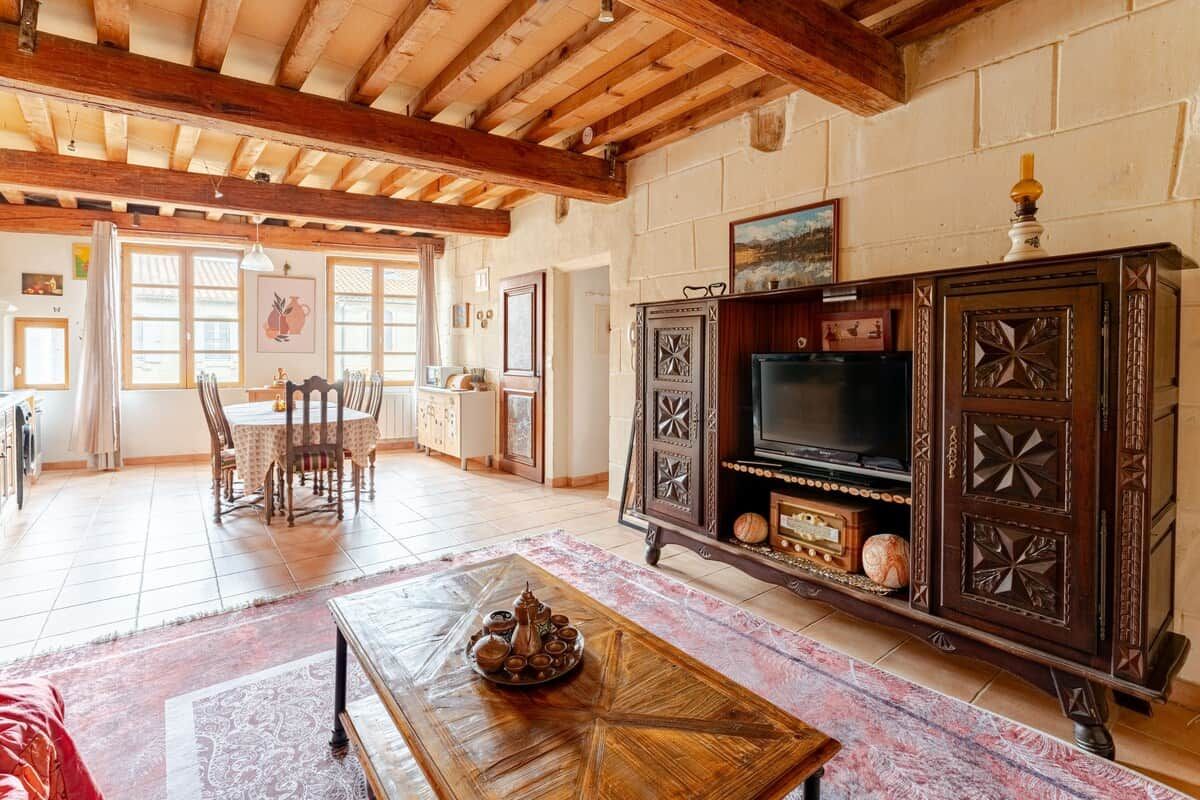 A spacious living area with a wooden ceiling, a television on a cabinet, and a dining table with chairs.