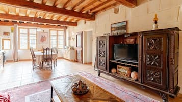 A spacious living area with a wooden ceiling, a television on a cabinet, and a dining table with chairs.