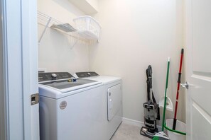 Ein Waschraum mit einer Waschmaschine und einem Trockner, einem Staubsauger und einem Mop.