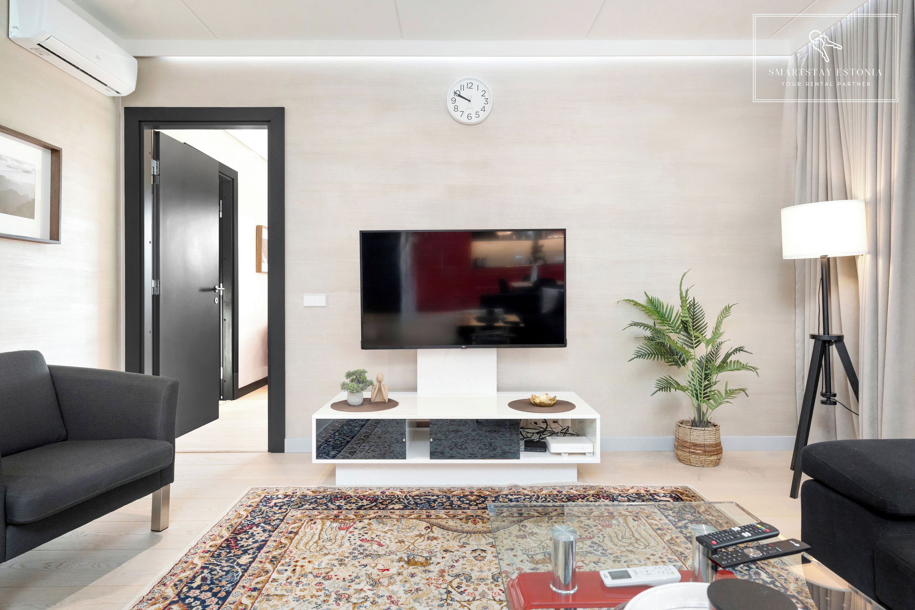 Een moderne woonkamer met een flatscreen televisie, een bank, een salontafel, een potplant en een lamp.