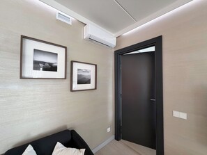 A modern room with a black door, two framed pictures on the wall, a black sofa, and an air conditioning unit.