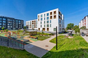 Un moderno edificio de apartamentos con parque infantil, zonas verdes y cielo despejado.