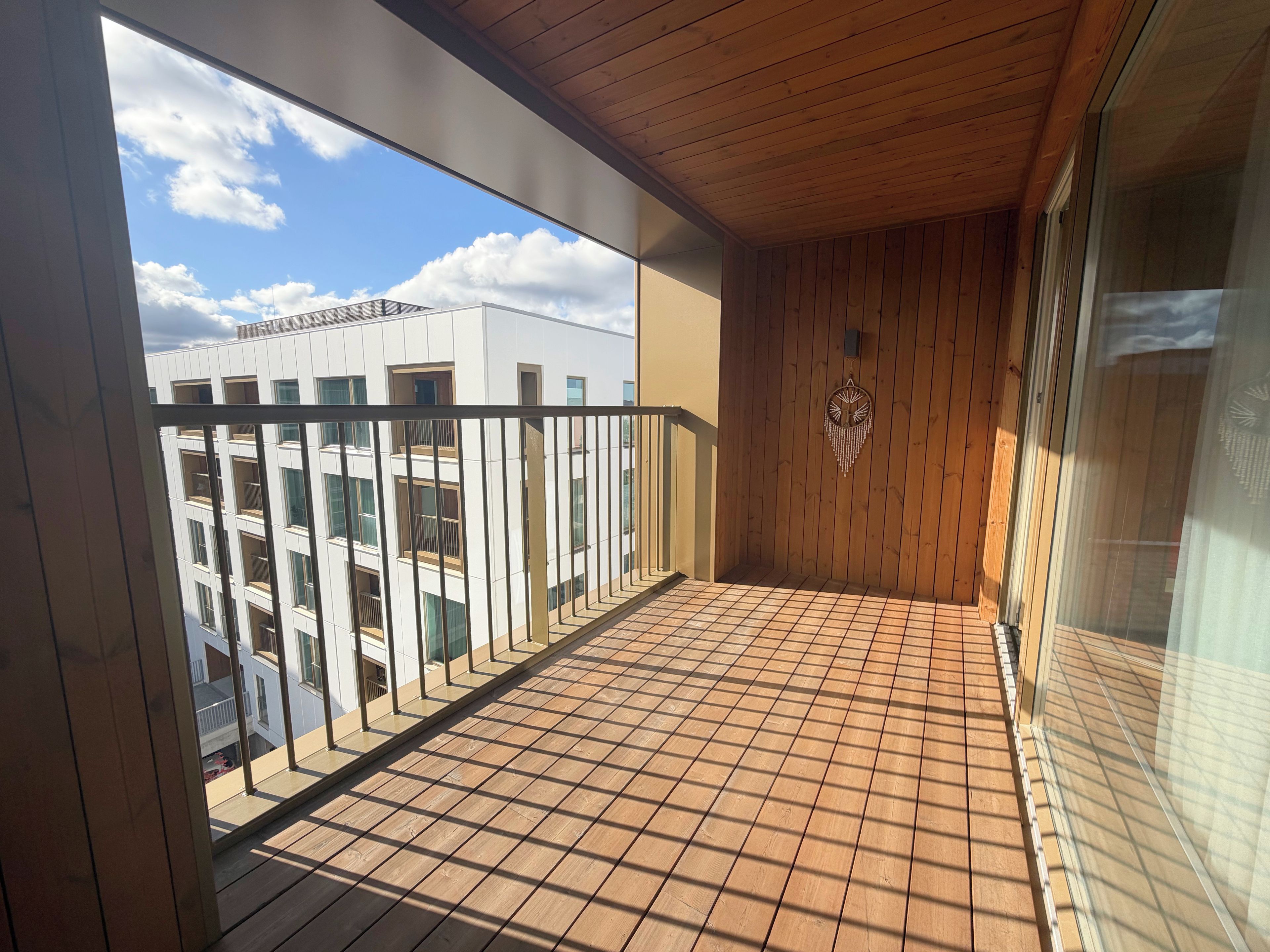 A balcony with a tiled floor, a wooden ceiling, and a view of a modern building.