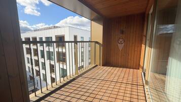 A balcony with a tiled floor, a wooden ceiling, and a view of a modern building.