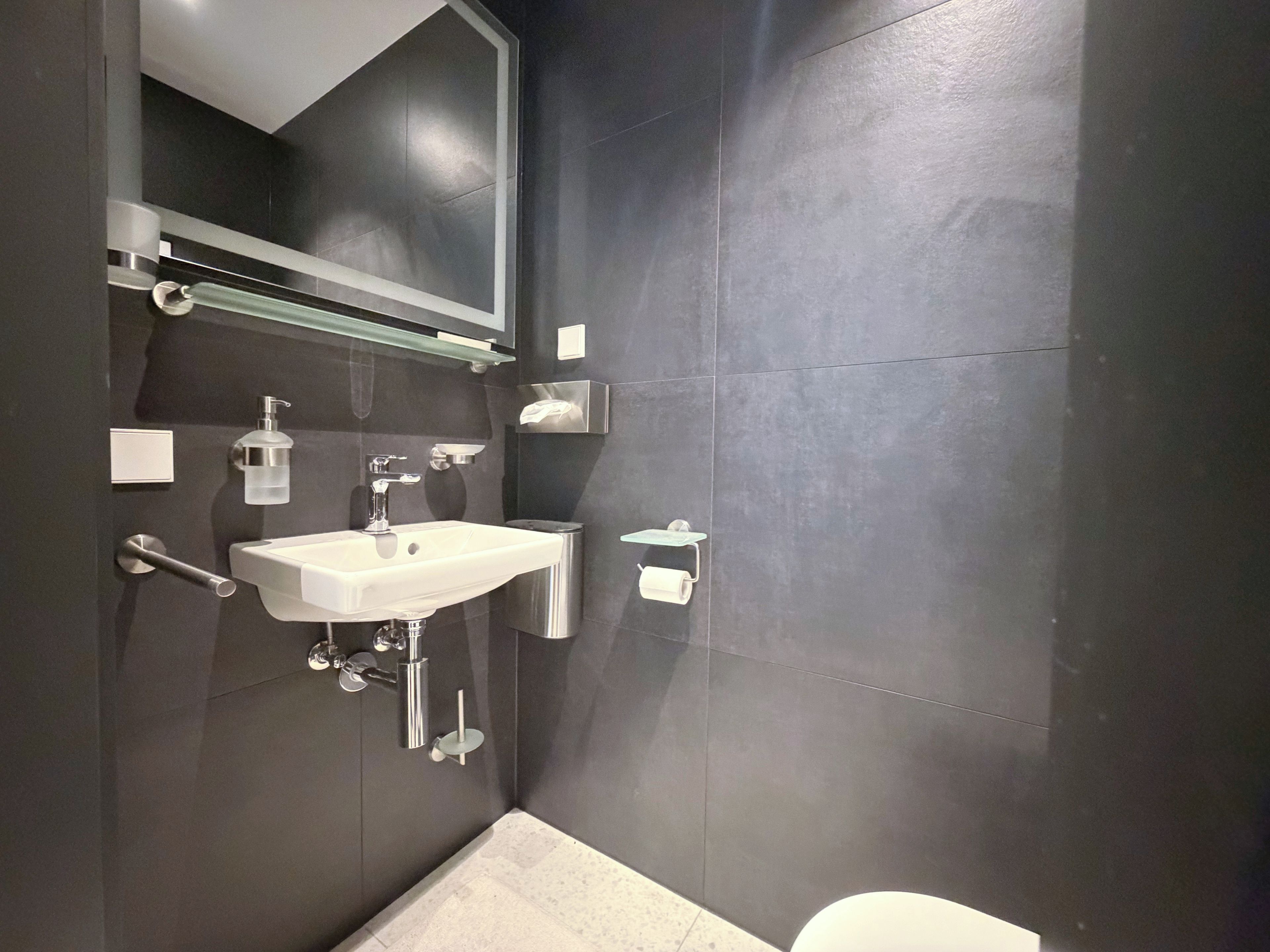 Ein modernes Badezimmer mit einem weißen Waschbecken, chromfarbenen Armaturen und einem Spiegel darüber.