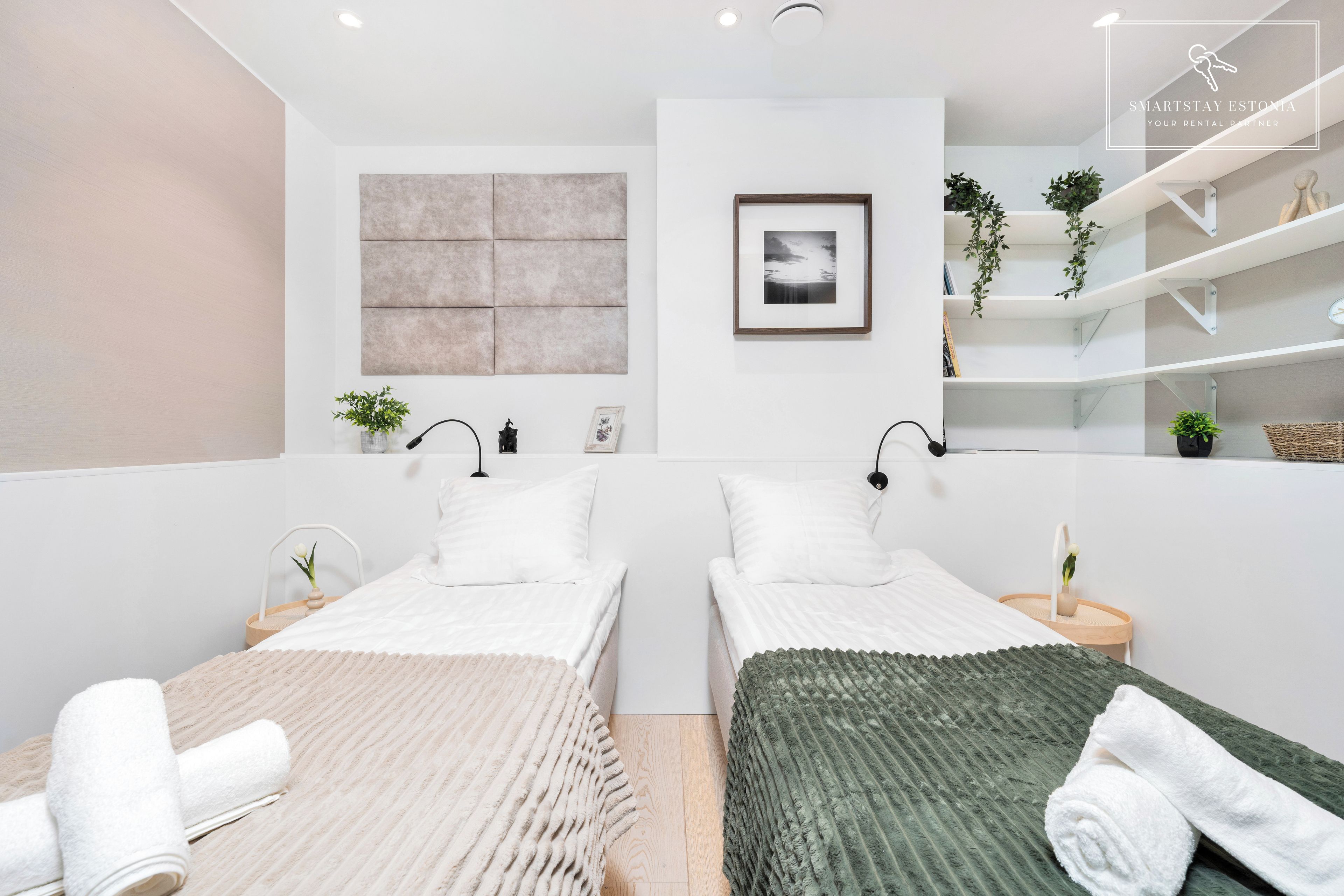 Une chambre moderne avec deux lits, une grande œuvre d’art accrochée au mur, un tableau encadré et une étagère avec des plantes.
