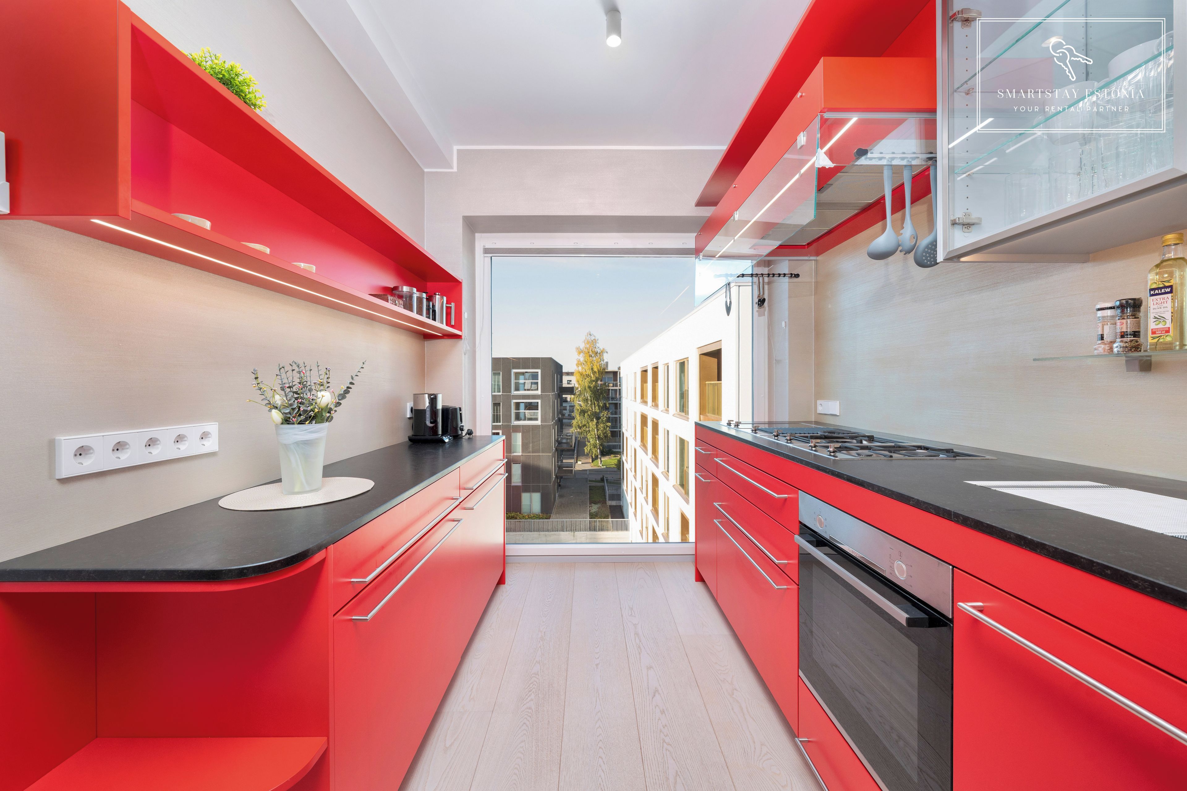 A modern kitchen with red cabinetry, a black countertop, and a view of the outside.