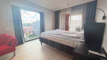 A modern bedroom with a large bed, a red chair, a desk, and a view of a building through a large window.