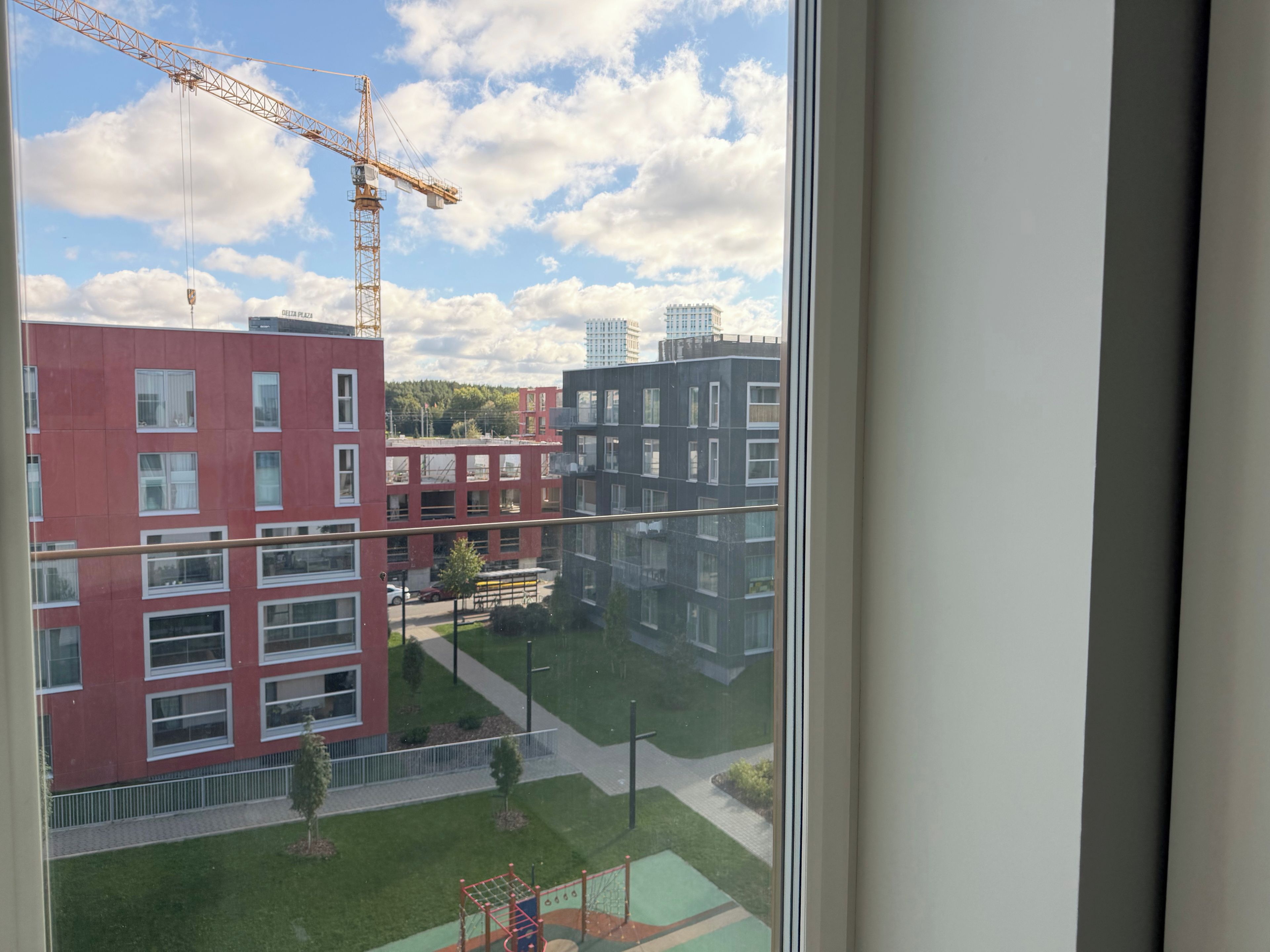 Blick aus einem Fenster auf eine Baustelle mit Kran, einen Spielplatz und moderne Gebäude.