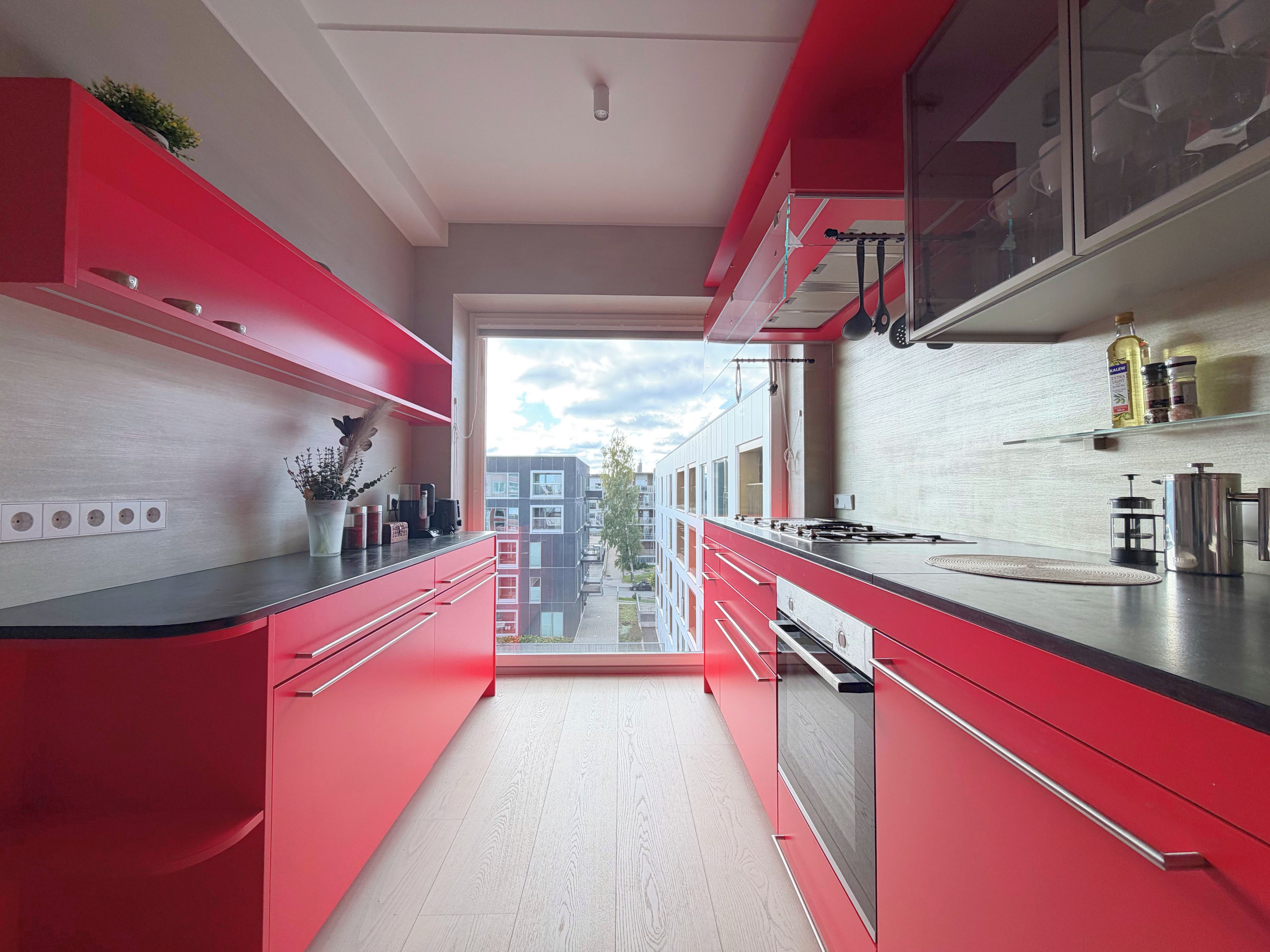 Una cocina moderna con armarios rojos, encimera negra y vista a un edificio a través de la ventana.