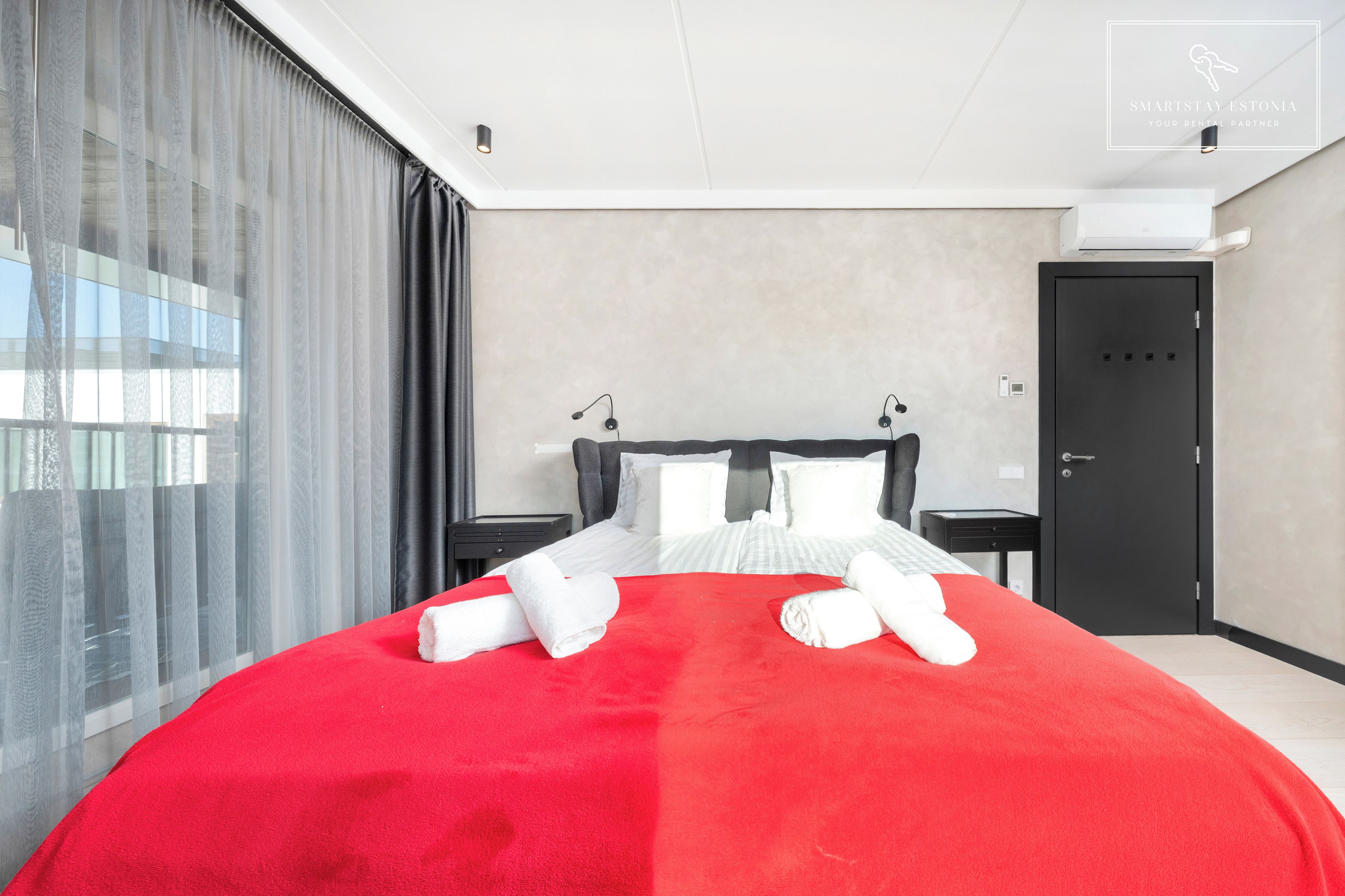 A hotel room with a large bed, a bedside table, a nightstand, a wardrobe, and a window with curtains.