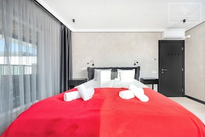 A hotel room with a large bed, a bedside table, a nightstand, a wardrobe, and a window with curtains.