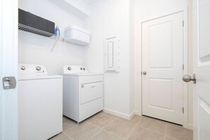 A laundry room with two washing machines, a drying rack, and a door. - 9BR Solara Home Pool, spa & Themed Rooms (Kissimmee)