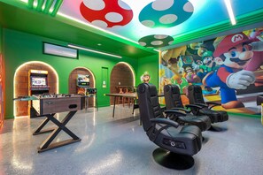 A room with green walls, a Mario-themed mural, a foosball table, and multiple gaming chairs. - 9BR Solara Home Pool, spa & Themed Rooms (Kissimmee)