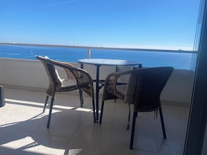 A balcony with two wicker chairs and a small round table, overlooking a clear blue sea. - Beautiful Beach Front Line Apartment, perfect central location. (Fuengirola)
