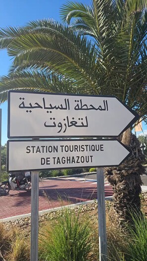 A directional sign with Arabic text and its English translation, pointing towards a tourist station. - Sea View Apt in Taghazout - Pool - Surf & Golf (Agadir)