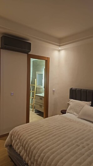A bedroom with a bed, a nightstand, and a door leading to a bathroom. - Sea View Apt in Taghazout - Pool - Surf & Golf (Agadir)