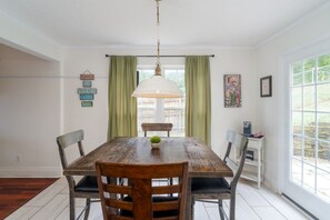 Ein Essbereich mit einem Holztisch, vier Stühlen, einer Pendelleuchte und Blick ins Freie durch ein Fenster.