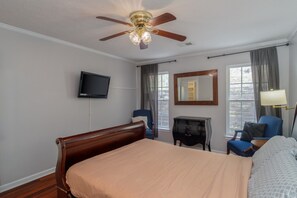Ein Hotelzimmer mit einem Bett, einem Fernseher, einem Schreibtisch, einem Stuhl, einem Spiegel und einem Deckenventilator.