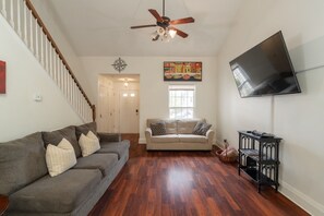 Ein Wohnzimmer mit grauem Sofa, beigem Sofa, Holzboden, Deckenventilator, Flachbildfernseher und einer Treppe.