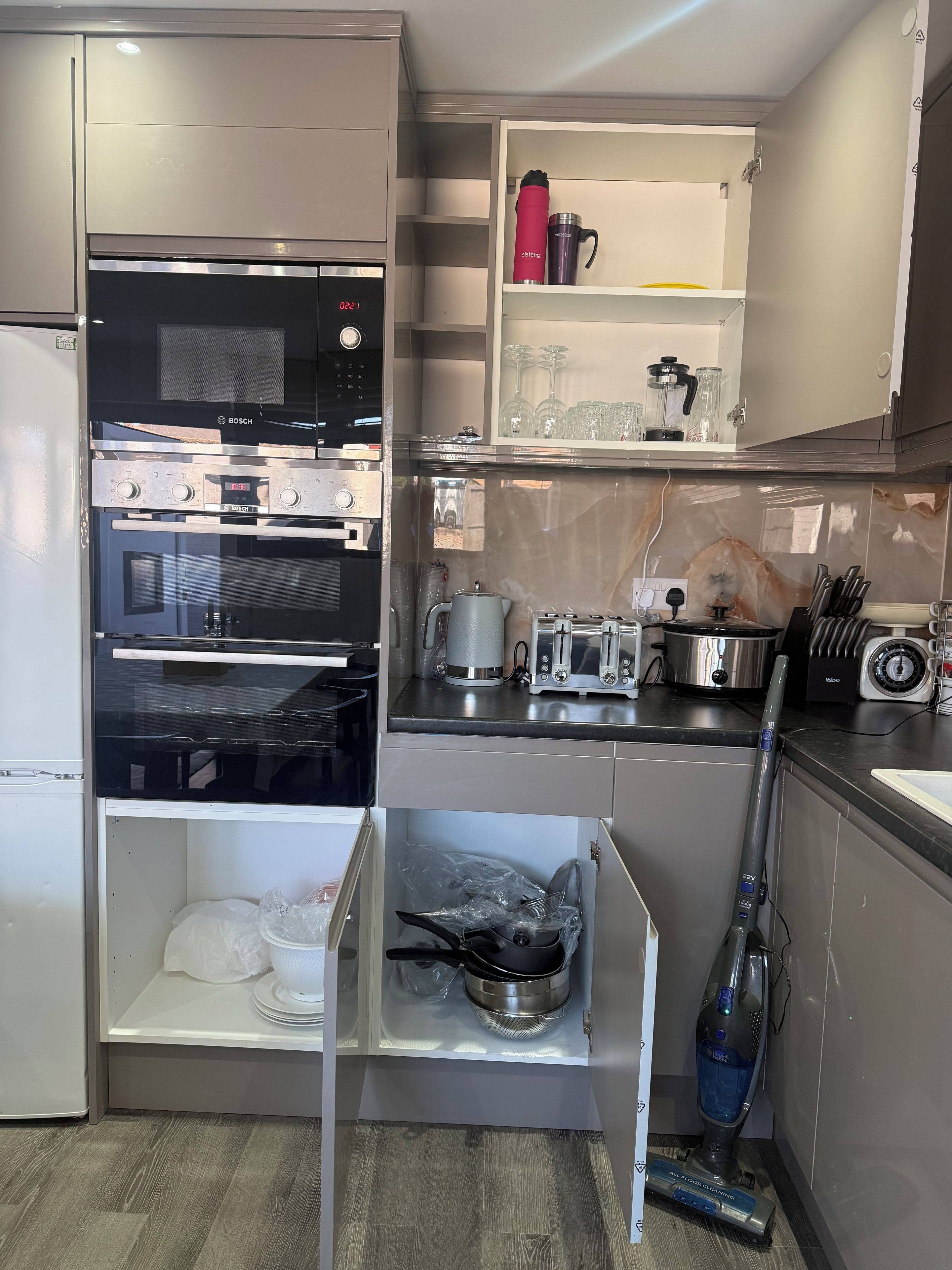 A modern kitchen with a Bosch oven, a microwave, a coffee maker, and a vacuum cleaner.