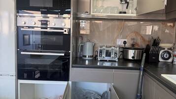 A modern kitchen with a Bosch oven, a microwave, a coffee maker, and a vacuum cleaner.
