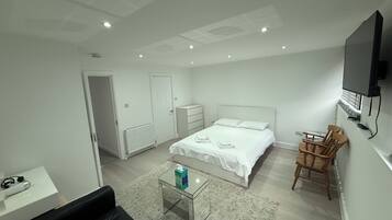 A modern bedroom with a bed, a desk, a chair, and a television.