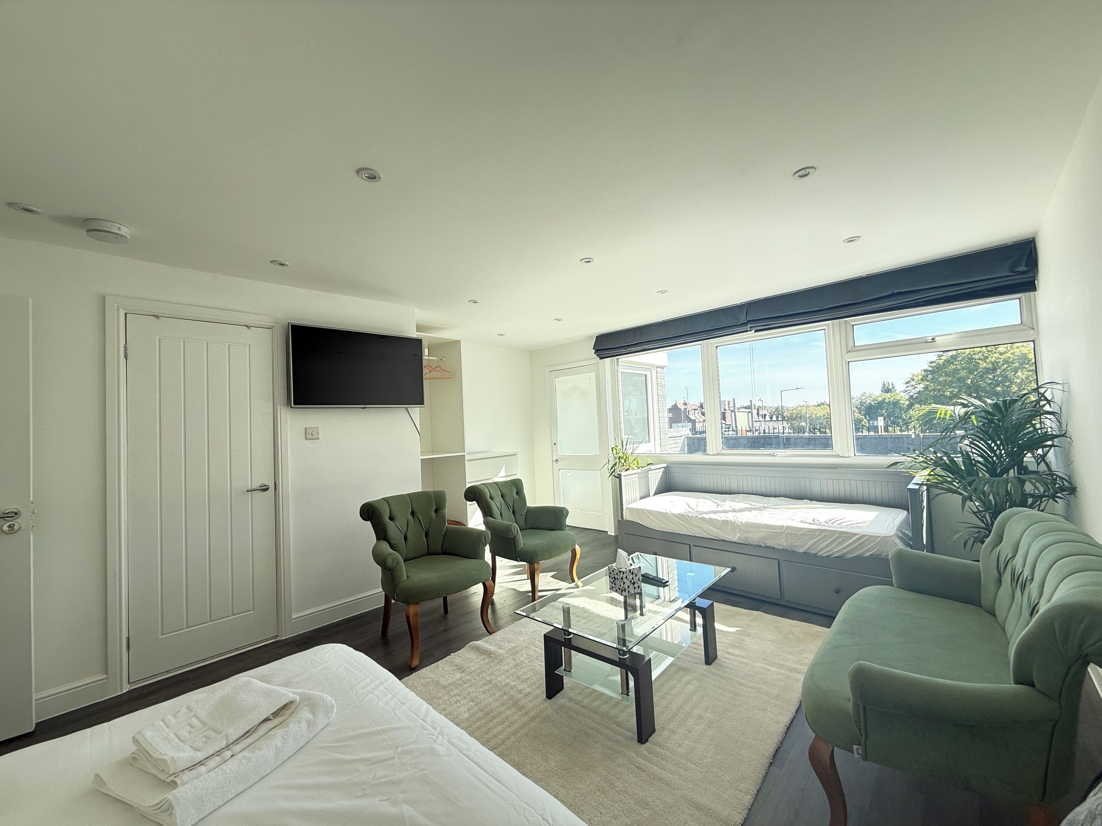 A modern hotel room with a bed, two armchairs, a sofa, a television, and a large window with a view.
