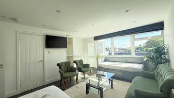 A modern hotel room with a bed, two armchairs, a sofa, a television, and a large window with a view.