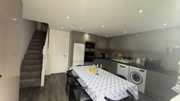 A compact kitchen with modern appliances, a dining area with a table and chairs, and a staircase leading to another level.