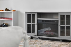 Une pièce avec une cheminée, un fauteuil blanc et une bibliothèque remplie de livres.