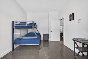 Une chambre avec un lit superposé, un bureau et une porte donnant sur une autre pièce.