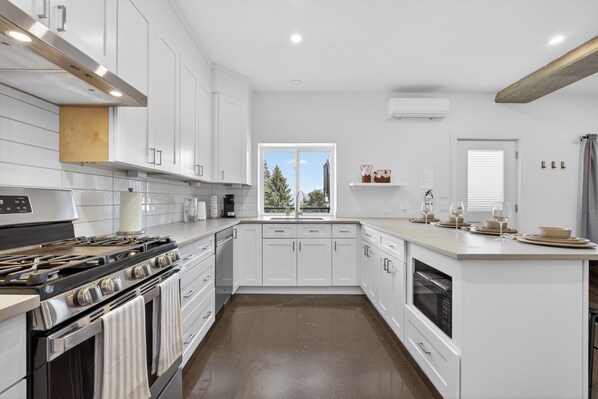 Una cocina moderna con armarios blancos, horno empotrado y ventana con vistas a árboles.